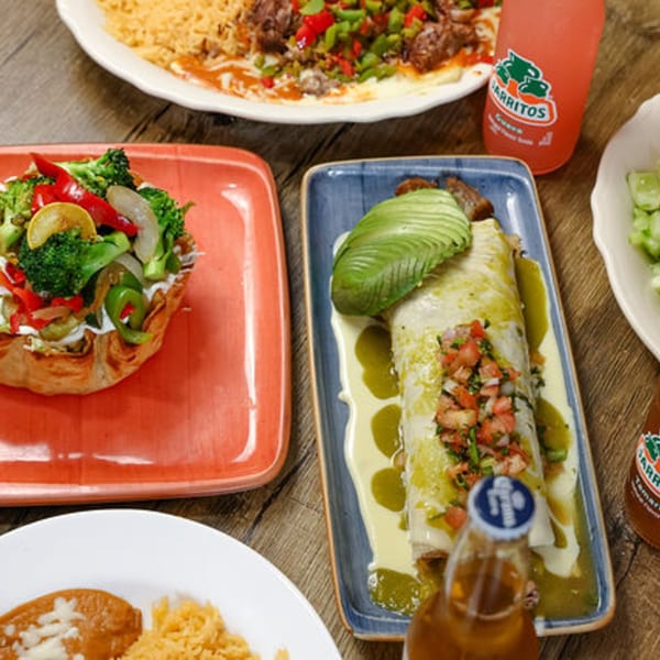 A table spread with various Mexican dishes, including a burrito, taco salad, and drinks.