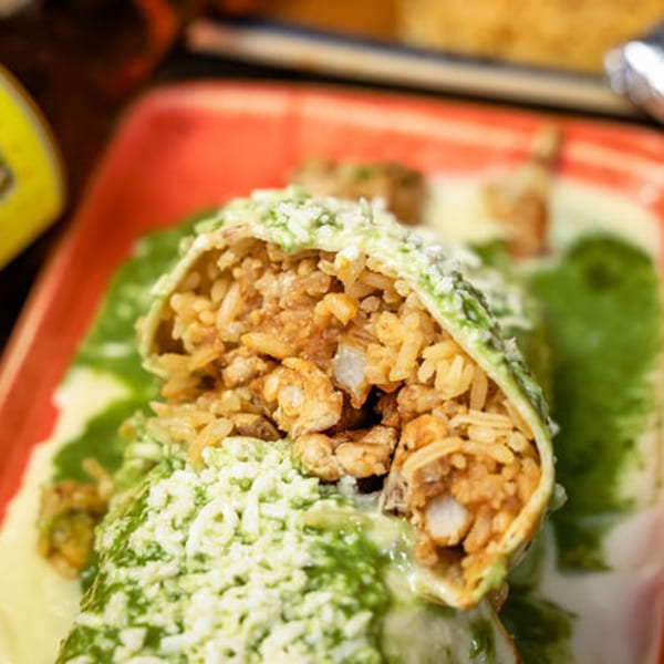 A close-up of a burrito cut in half, revealing rice and meat, covered in green sauce and cheese.