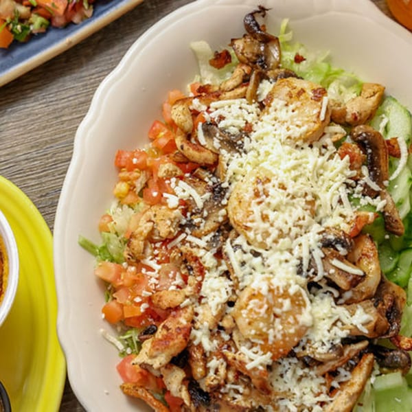 A large white bowl filled with a salad of chicken, mushrooms, tomatoes, and shredded cheese.